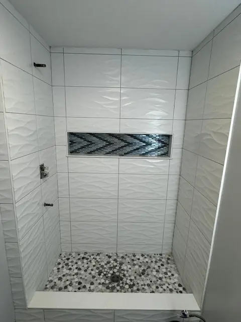 Walk-in shower with textured white wall tile, chevron niche and pebble floor