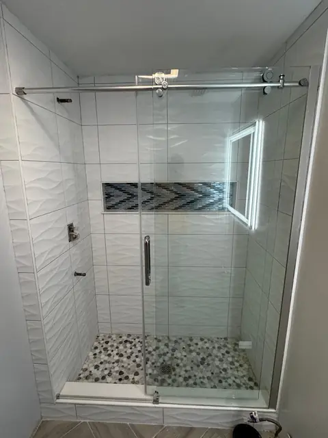 Walk-in shower with frameless sliding glass door and pebble shower floor