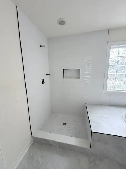 Walk-in shower with wavy white wall tile, a framed mosaic niche and a pebble-look floor beside the tub deck