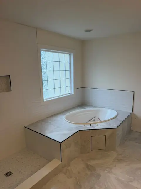 Corner tub deck wrapped in marble-look porcelain tile with a tiled access panel, tile done before fixtures