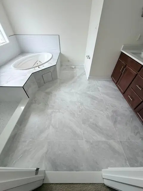 Marble-look porcelain tile floor running from the tiled corner tub deck to the vanity