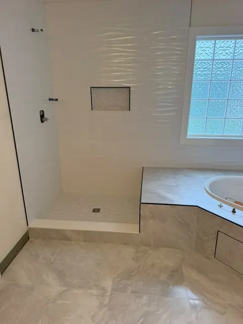 Walk-in shower with wavy white wall tile, marble mosaic niche and floor, next to a tiled tub deck
